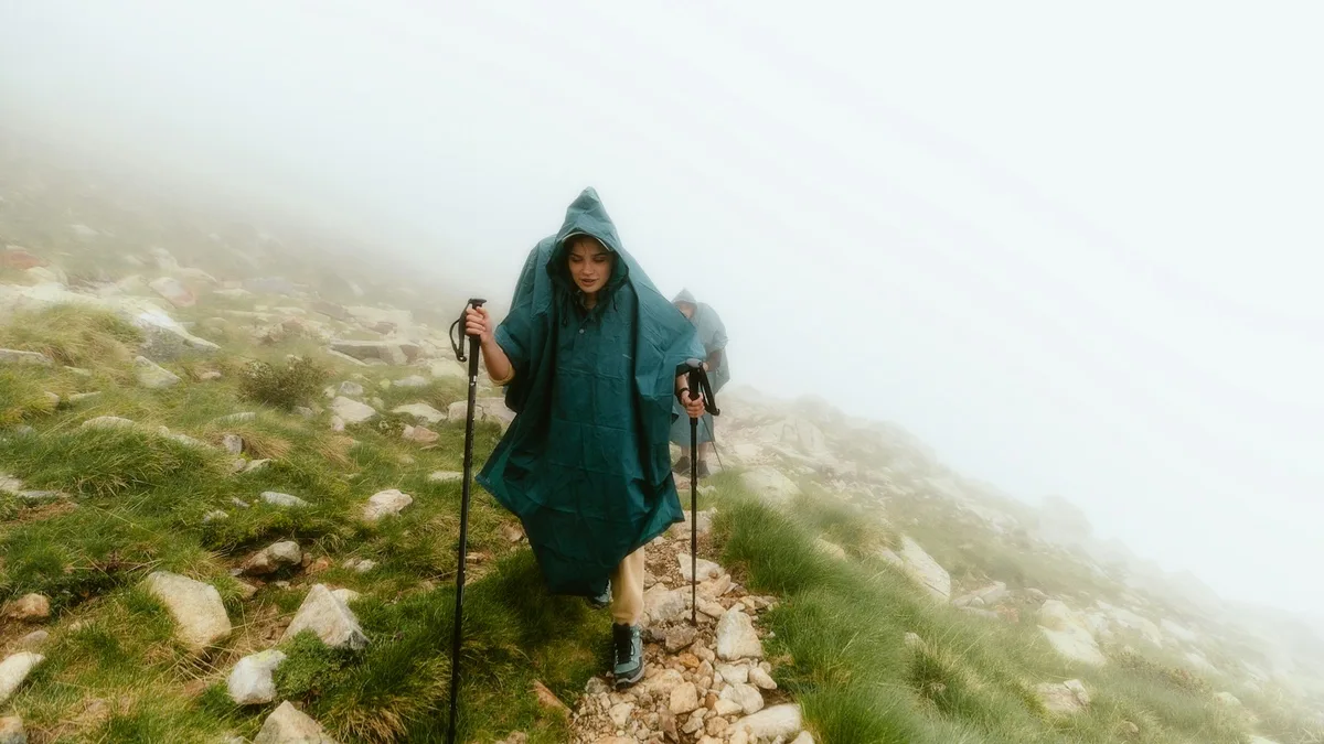 A pilgrim in a hooded jacket walking up a hill in changeable weather
